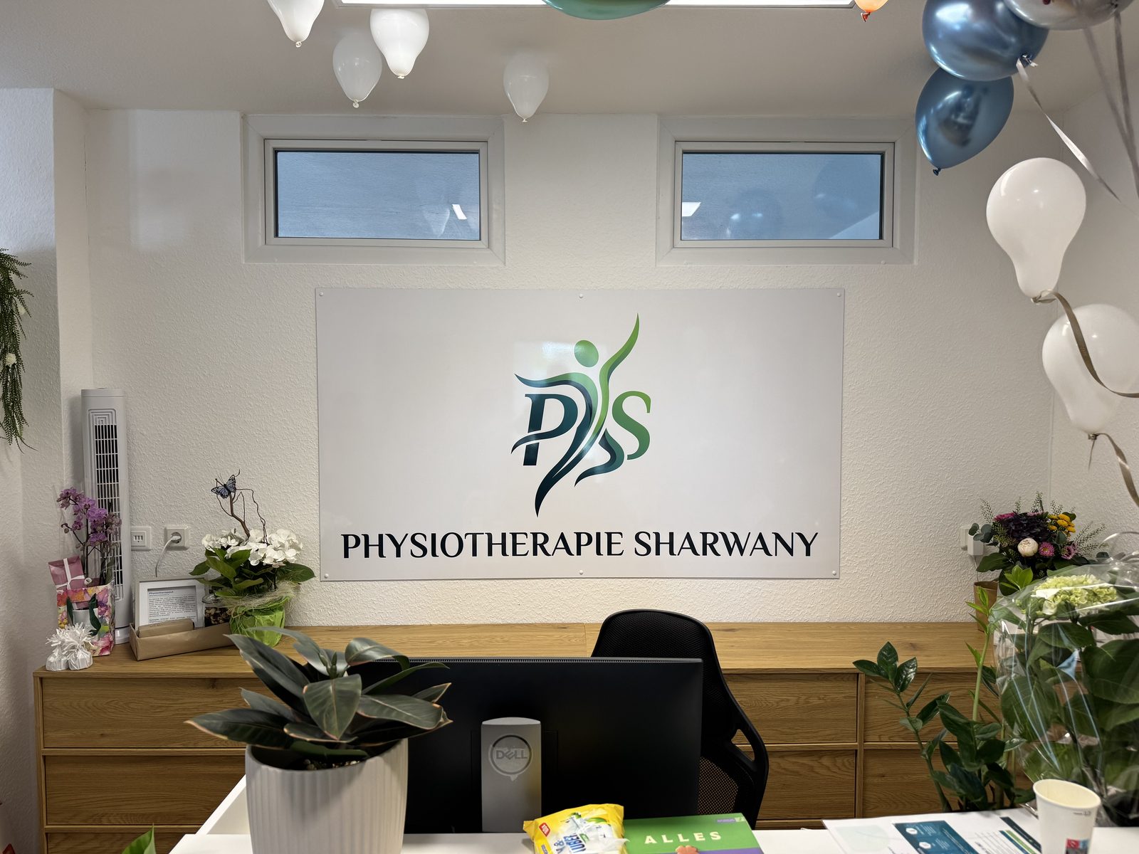 Empfangsbereich der Physiotherapie Sharwany mit Logo an der Wand, Blumen und Luftballons